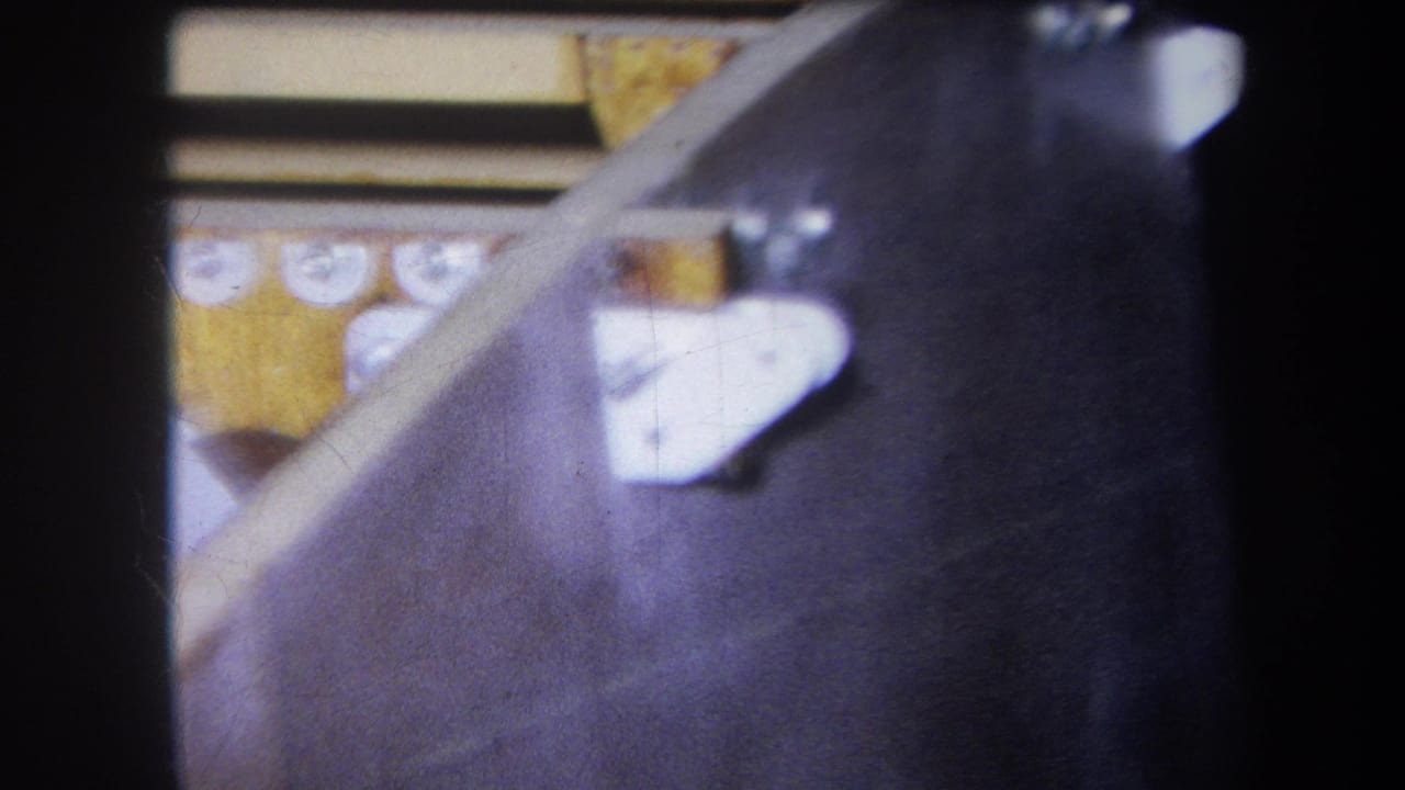 Dark sloped machine surface with white bracket pieces and yellow parts in the background.