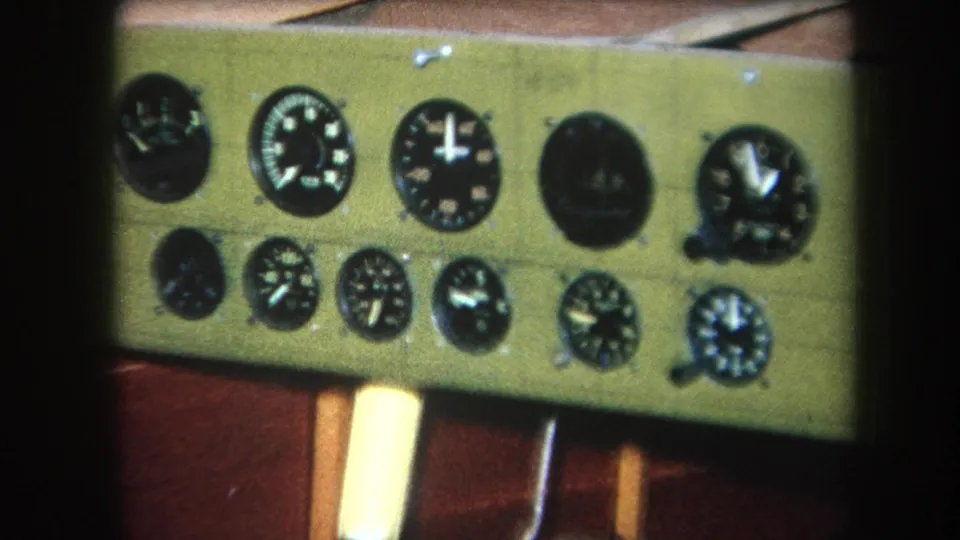 1964 8mm close-up of a greenish electronic instrument panel with two rows of analog gauges and a pale vertical handle below.