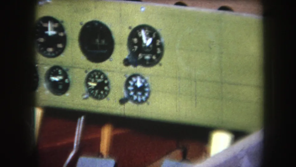 1964 home-movie frame showing the right portion of a green wooden dashboard with round black gauges and soft focus.