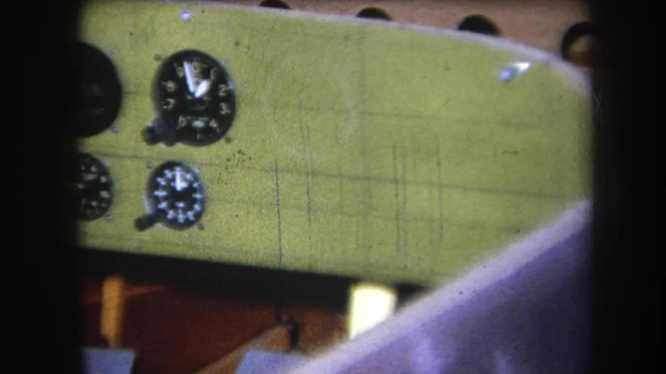 1964 home-movie frame with a cropped view of the green painted dashboard, showing gauges along the left edge and wood structure below.