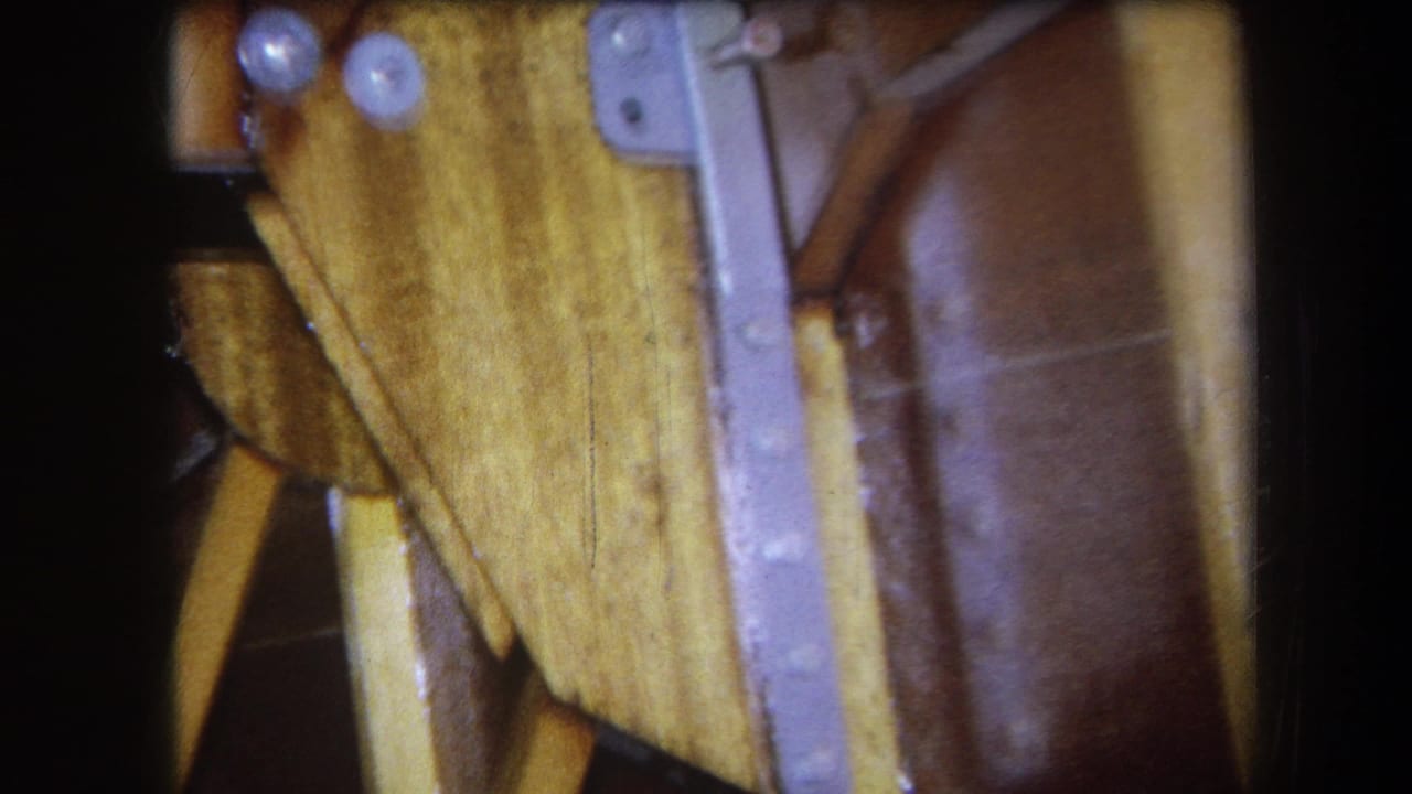 1964 Yucaipa frame with the camera close to a table's underside, showing a metal brace, fasteners, pale wood, and a brown surface.