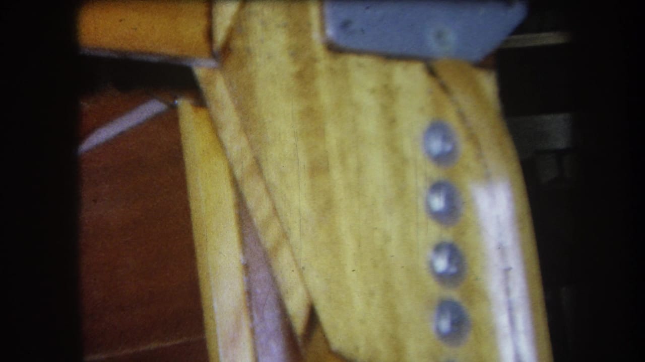 Close 1964 Yucaipa frame of varnished wooden furniture underside, showing metal screw heads, a gray bracket, and adjacent wood grain.