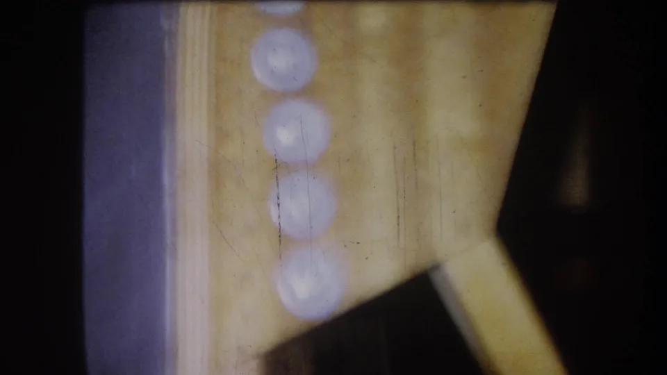 1964 8mm close view inside a mechanical interior, with blurred round highlights and an angled pale support visible at right.