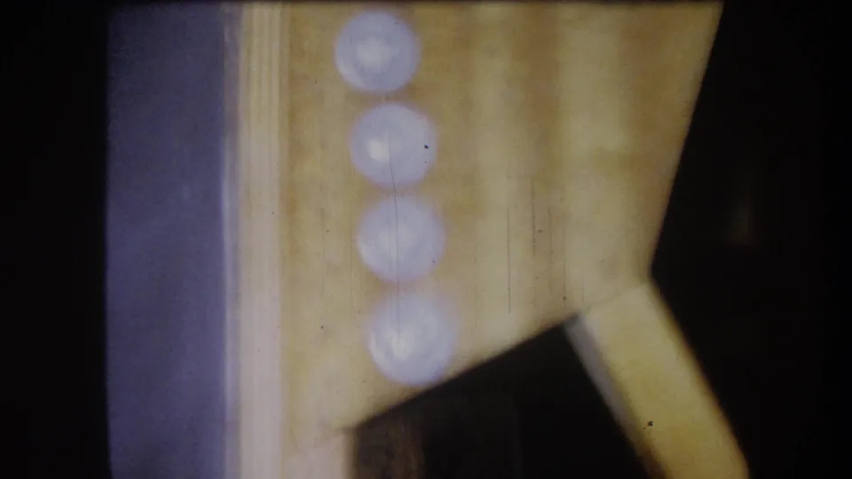 1964 Volmer Yucaipa 8mm frame showing a soft close-up of a panel area with circular highlights and a diagonal support piece.