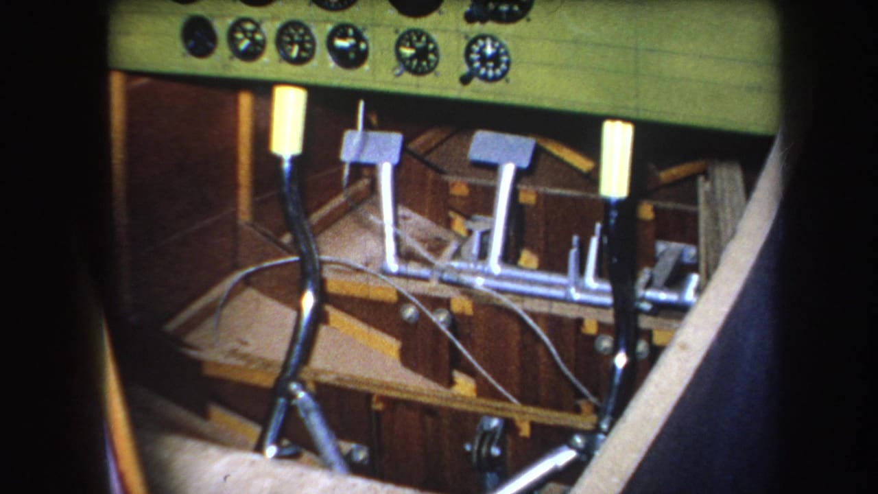 1964 Yucaipa-area 8mm frame showing a small aircraft cockpit with green instrument panel, round gauges, control levers, pedals, and wood cabin surfaces.