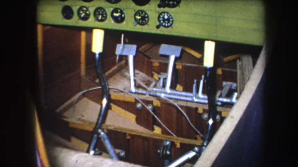 1964 Yucaipa-area 8mm frame showing a small aircraft cockpit with green instrument panel, round gauges, control levers, pedals, and wood cabin surfaces.