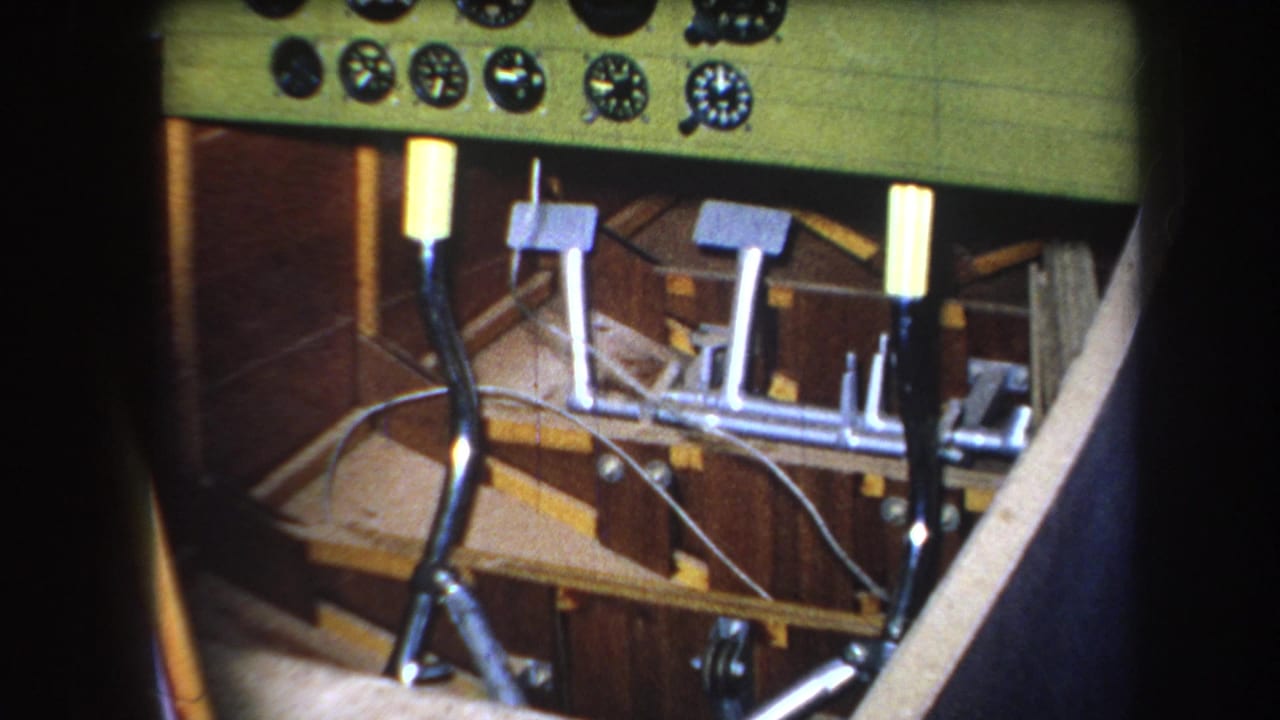 Aircraft dashboard with round gauges above metal pedals and control rods.