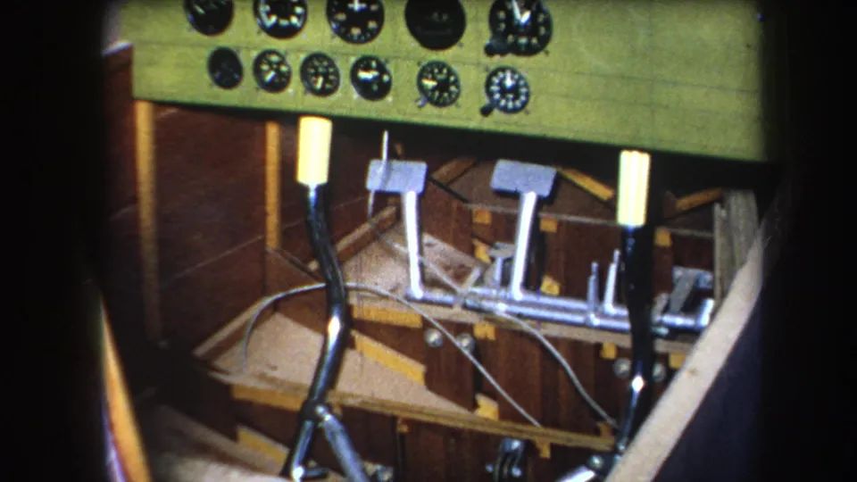 1964 8mm frame showing the lower cockpit area in Yucaipa, California, with dials along the top edge, metal pedals, joystick, wiring, and wood framing.