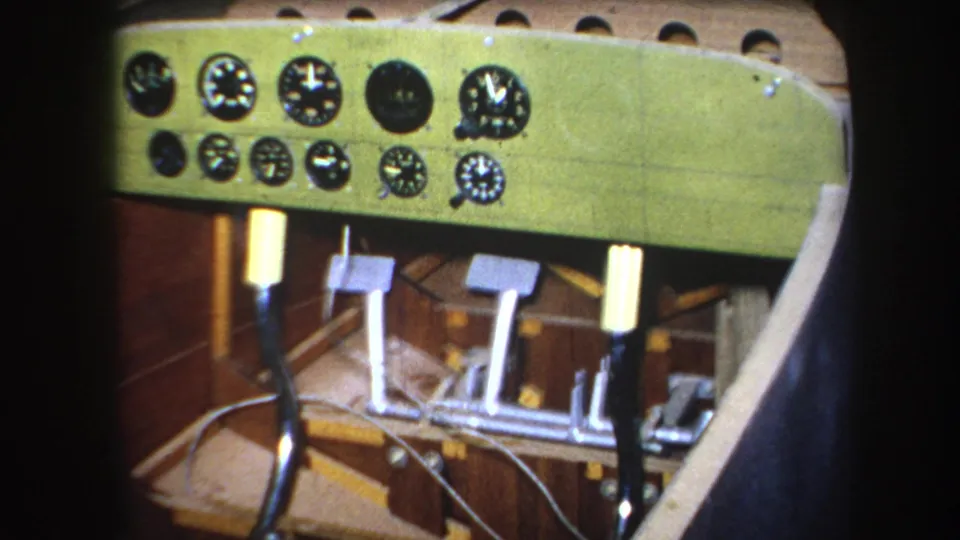 Final 1964 8mm frame from Yucaipa, California, showing analog cockpit instruments above pedals and a joystick within a wooden aircraft interior.
