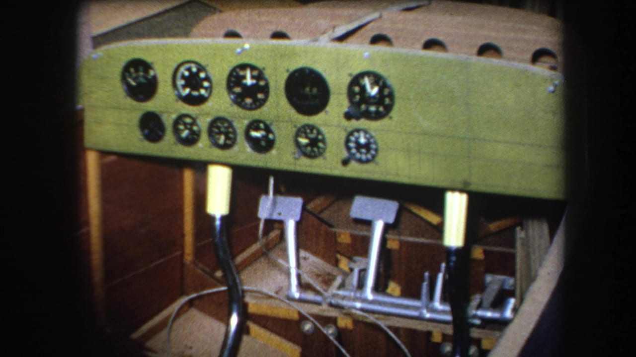 Cockpit panel with multiple round gauges, pedals, cables, and wooden structure below.