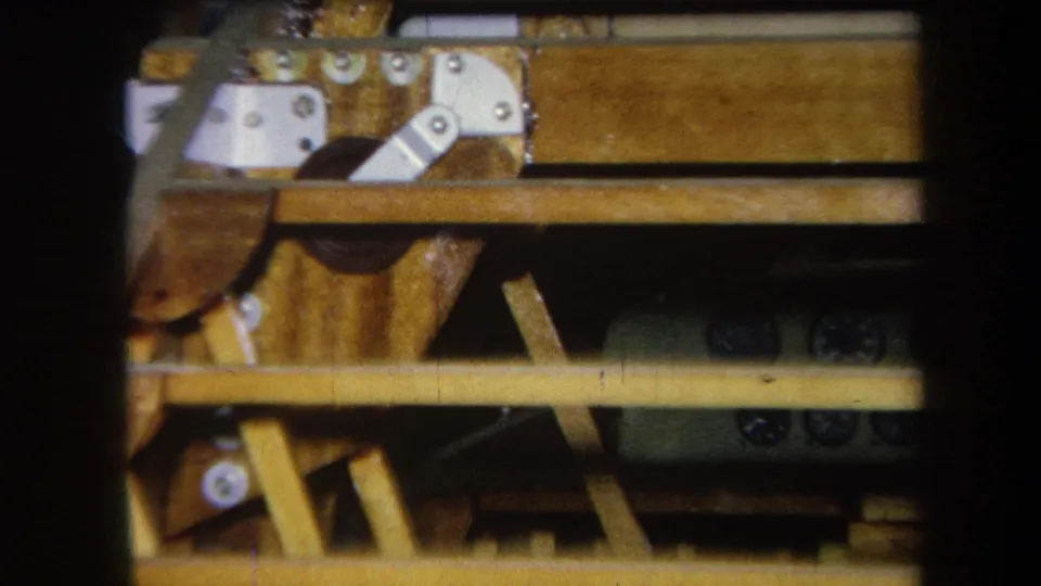 1964 Volmer Yucaipa frame showing internal wood framing with metal brackets, horizontal beams, dark openings, and warm 8mm color.