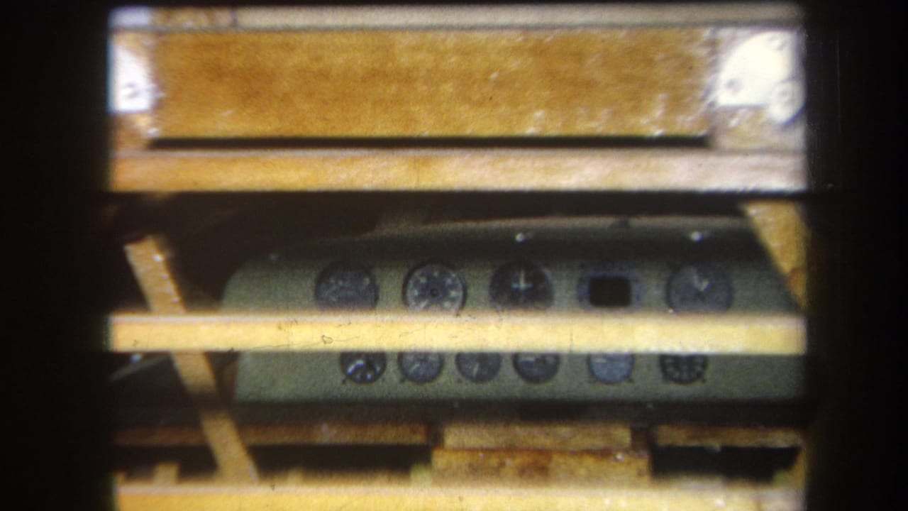 Close 8mm frame of a green-gray control panel under a wooden table in the 1964 Yucaipa footage.