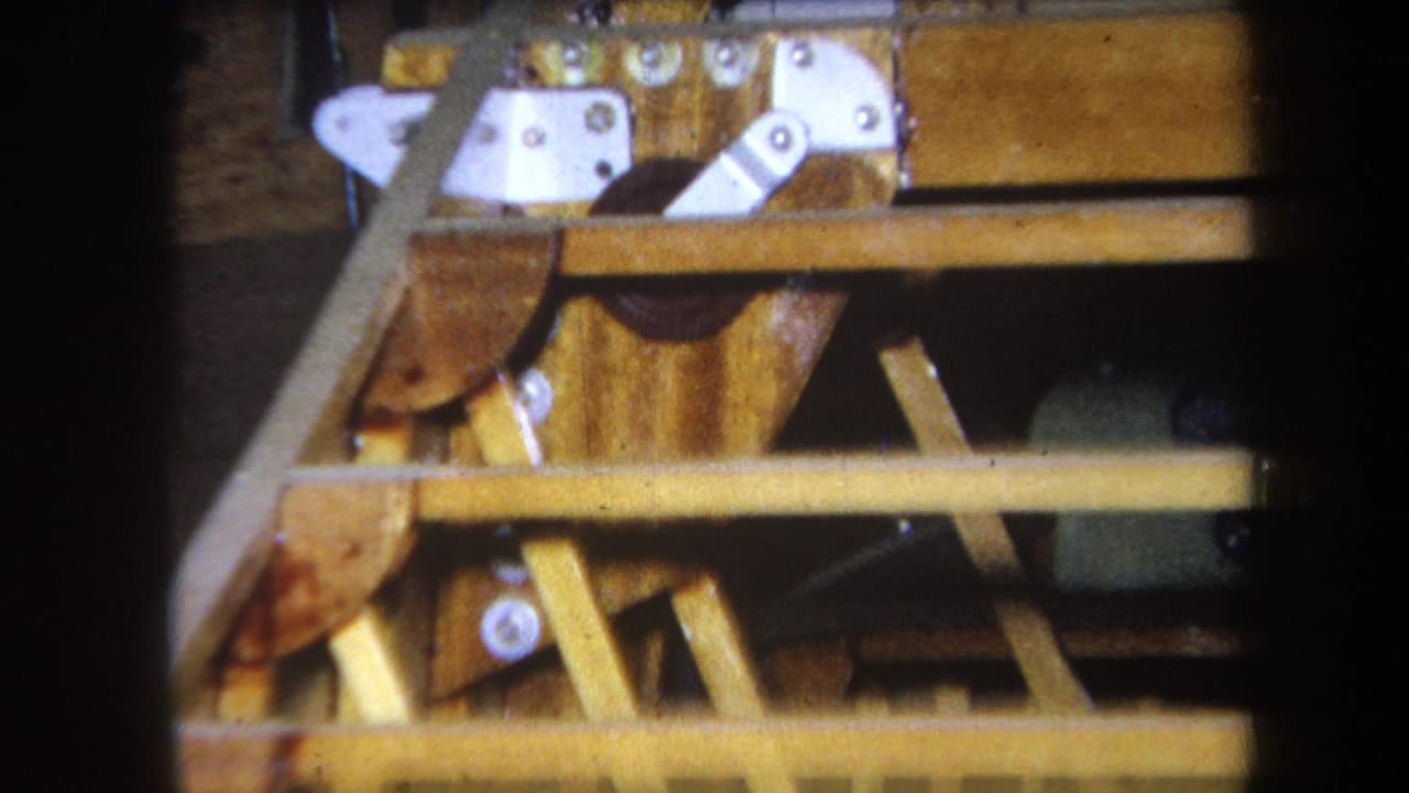 Close 1964 home-movie view of wood beams, pale metal brackets, and a partly obscured yellow gauge panel.