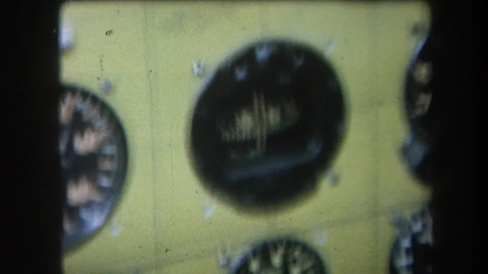 1964 home-movie frame showing a yellow analogue control panel with multiple circular dials, soft focus, and visible 8mm film texture.