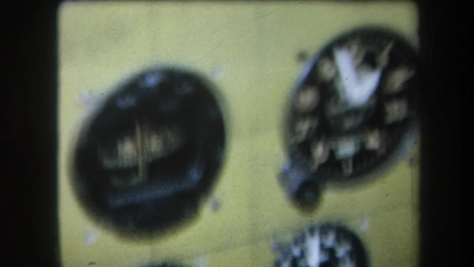 Later 1964 8mm frame with the yellow instrument panel slightly shifted, showing a dark round dial and a partial gauge at right.