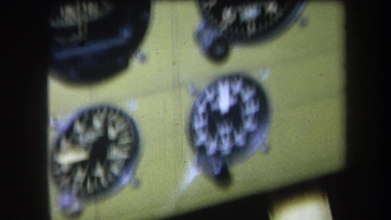 1964 8mm frame from Volmer Yucaipa showing a blurred close view of analog aircraft gauges on a yellow-green cockpit panel.