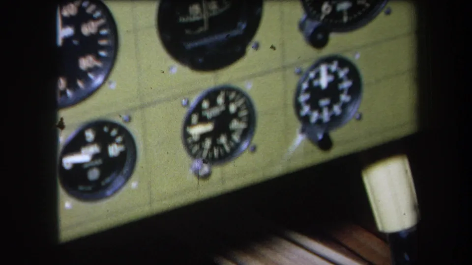 1964 Volmer Yucaipa 8mm frame showing a clearer aircraft instrument panel with several analog gauges and a light-colored lower knob.
