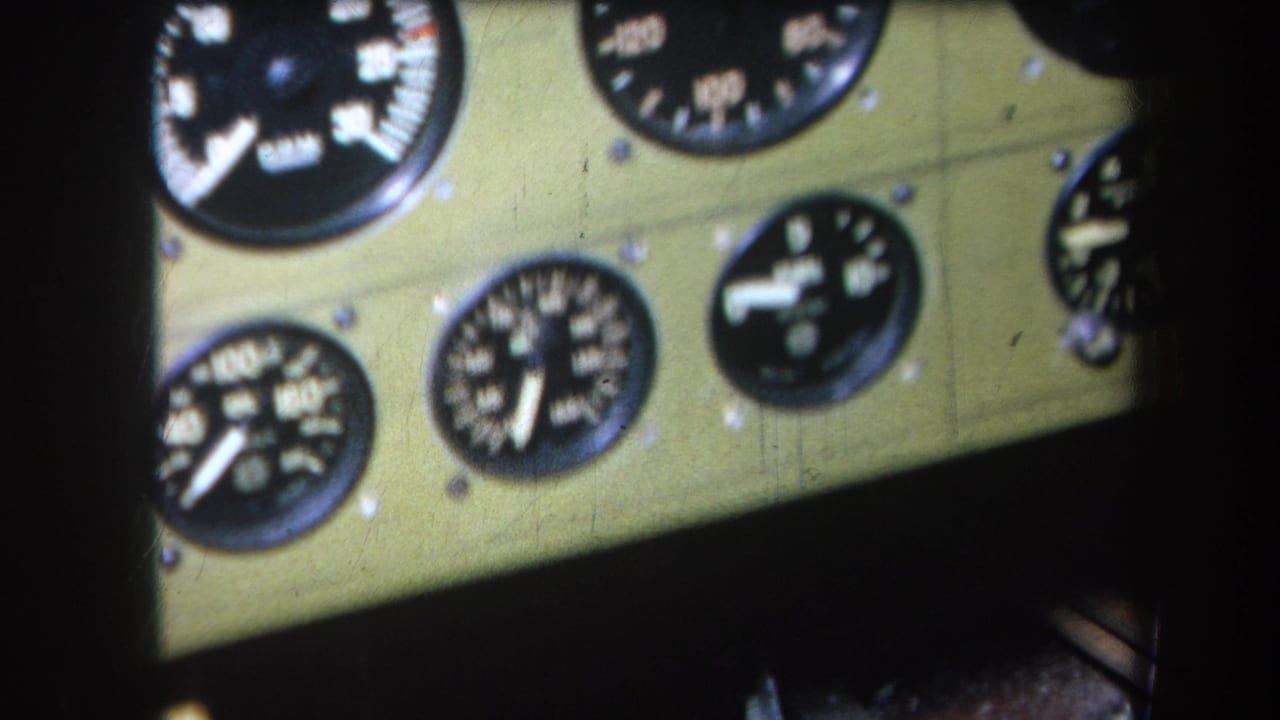1964 home-movie frame showing a green cockpit panel with black round flight gauges, white numerals, and visible mounting screws.