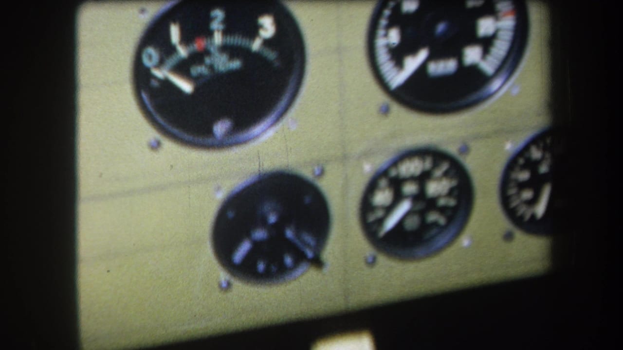 Close 1964 home-movie view of analog aircraft or machinery gauges with white markings on a khaki-colored panel.