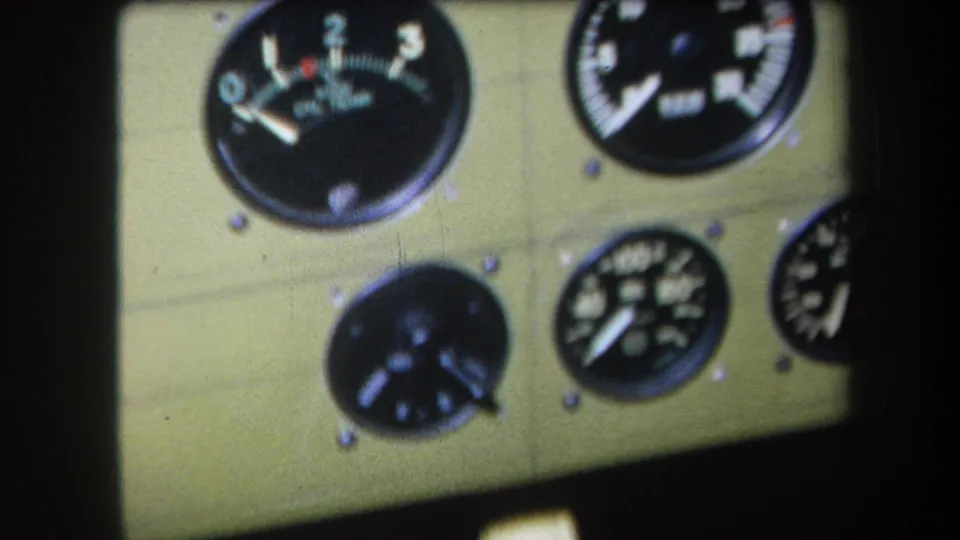 Close 1964 home-movie view of analog aircraft or machinery gauges with white markings on a khaki-colored panel.