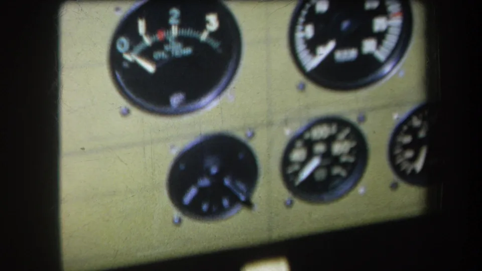 1964 8mm frame showing five round gauges on a khaki panel, with visible grain, blur, and shadowed frame edges.