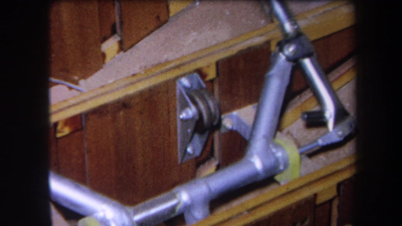 Close view of metal tubing and pulley-like hardware mounted against wood panels.