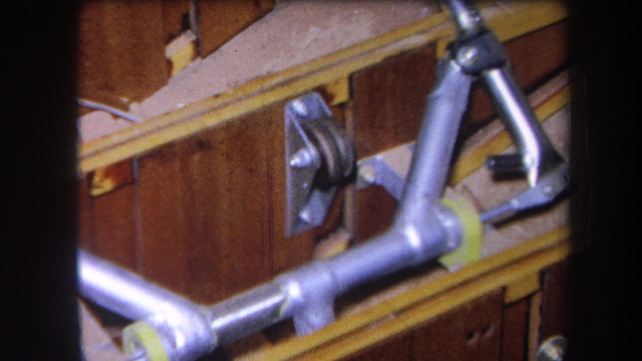 Close 1964 home-movie view of a silver metal frame, bracket, and yellow strip fixed to a wooden surface in Yucaipa.