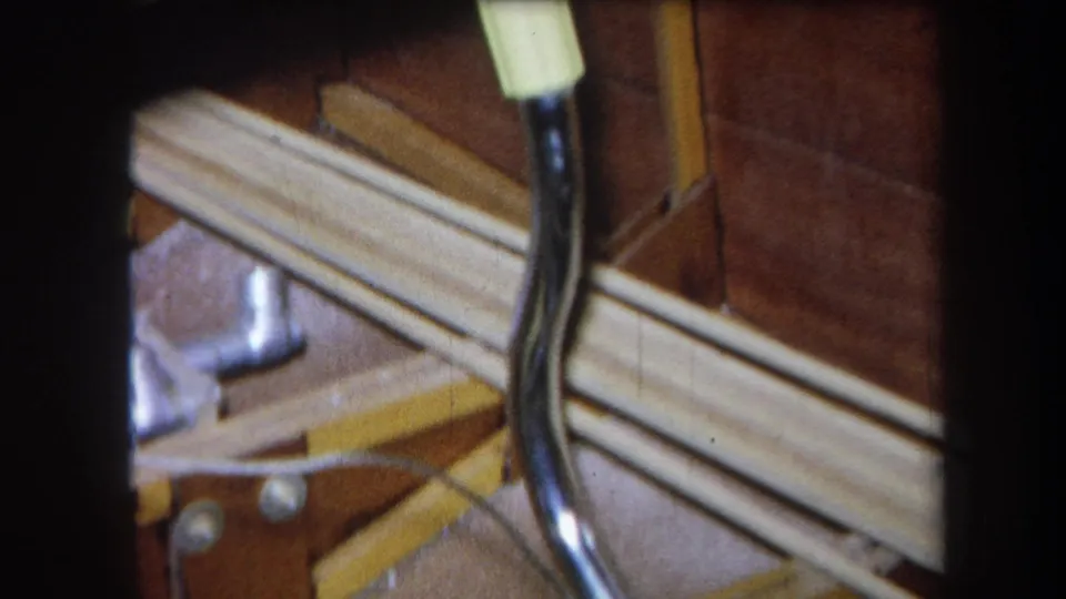 1964 Yucaipa home-movie frame showing cables, narrow rails, wooden paneling, and a partial metal bracket in close-up.