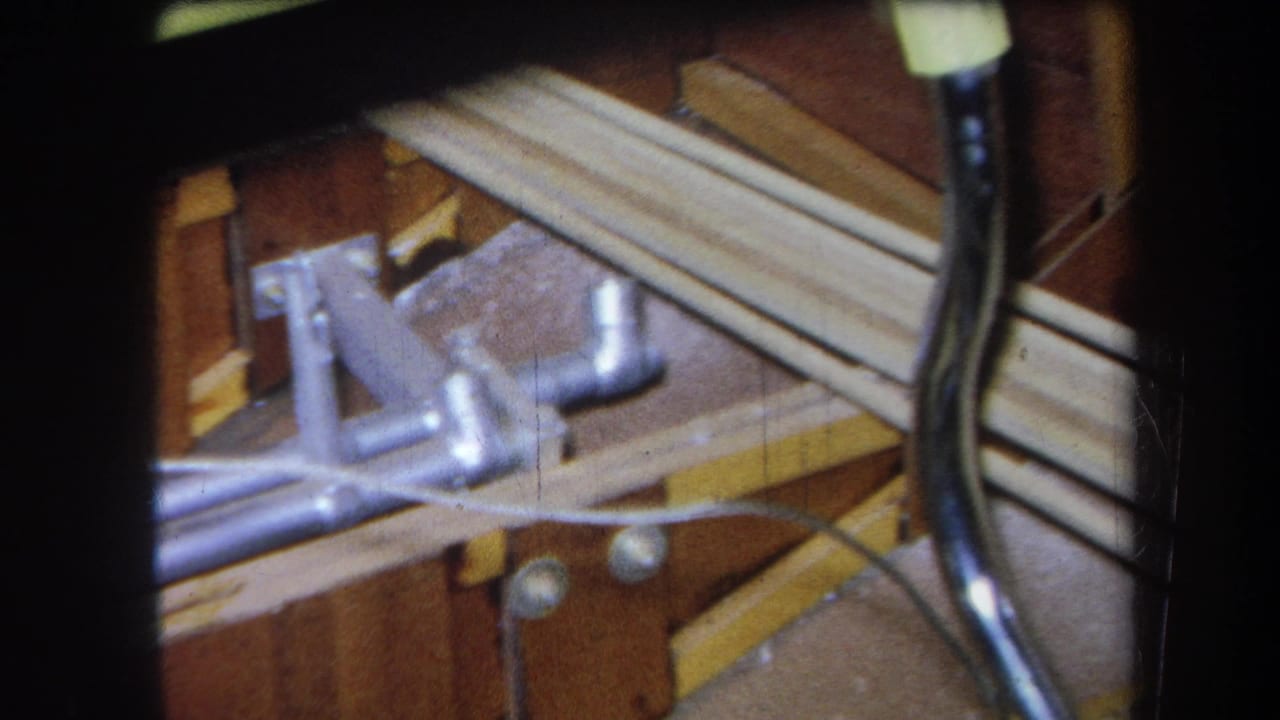 1964 Yucaipa frame showing a silver joystick-like mechanism, metal rods, bolts, and wooden framing in close-up.