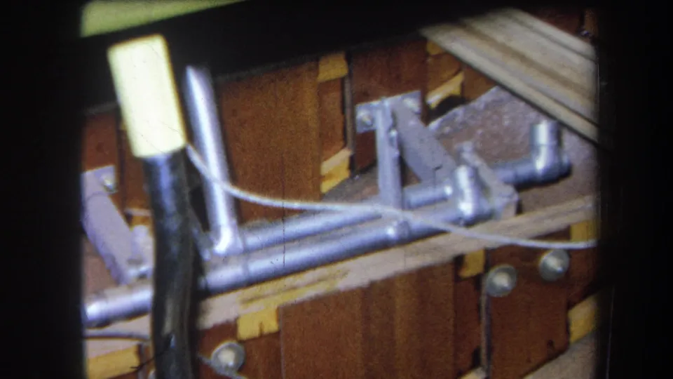 1964 Yucaipa home-movie frame with a metal control linkage, black cable, bolts, and wooden board-mounted hardware.