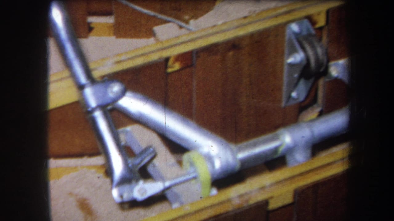 Metal pipe joint and bracket mounted beside yellow rails and brown panels.