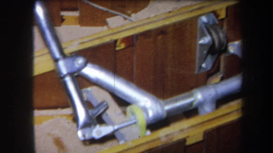 Close 1964 Yucaipa view of a silver pipe assembly fixed near yellow wooden rails and brown panel boards.