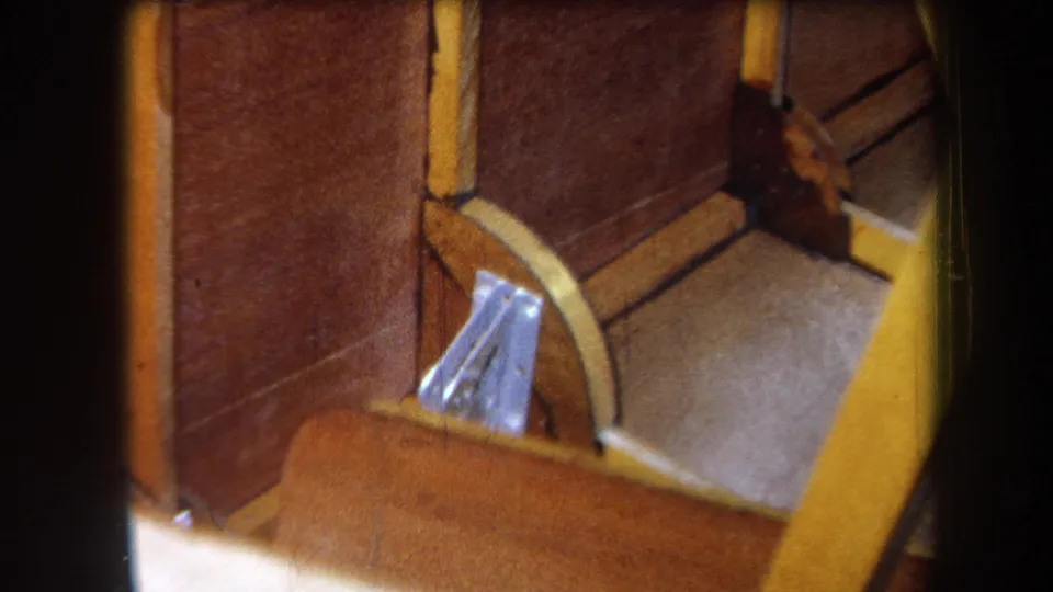 1964 Yucaipa home-movie view of a brown wooden compartment, yellow trim, curved support, and small metal bracket.