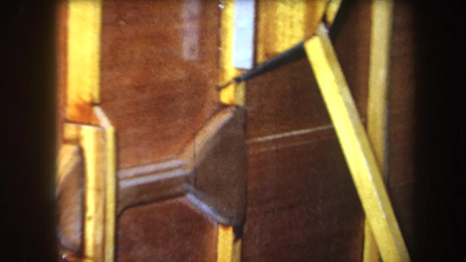 1964 Yucaipa 8mm frame showing yellow structural strips across brown wood panels, with a darker shaped joint or support near the center.