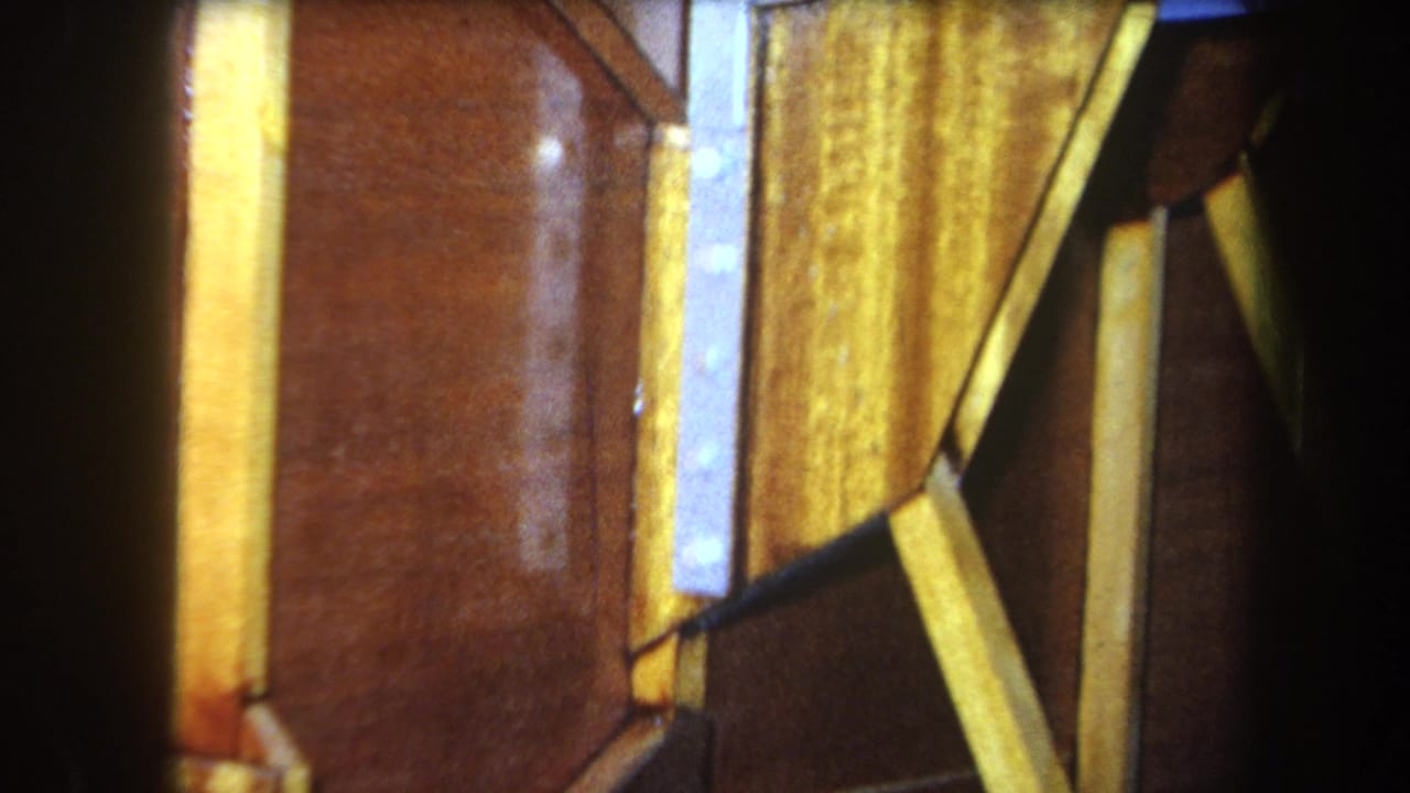 1964 8mm close-up from Yucaipa showing yellow wood boards, a brown panel, and shadowed gaps in a small structure.