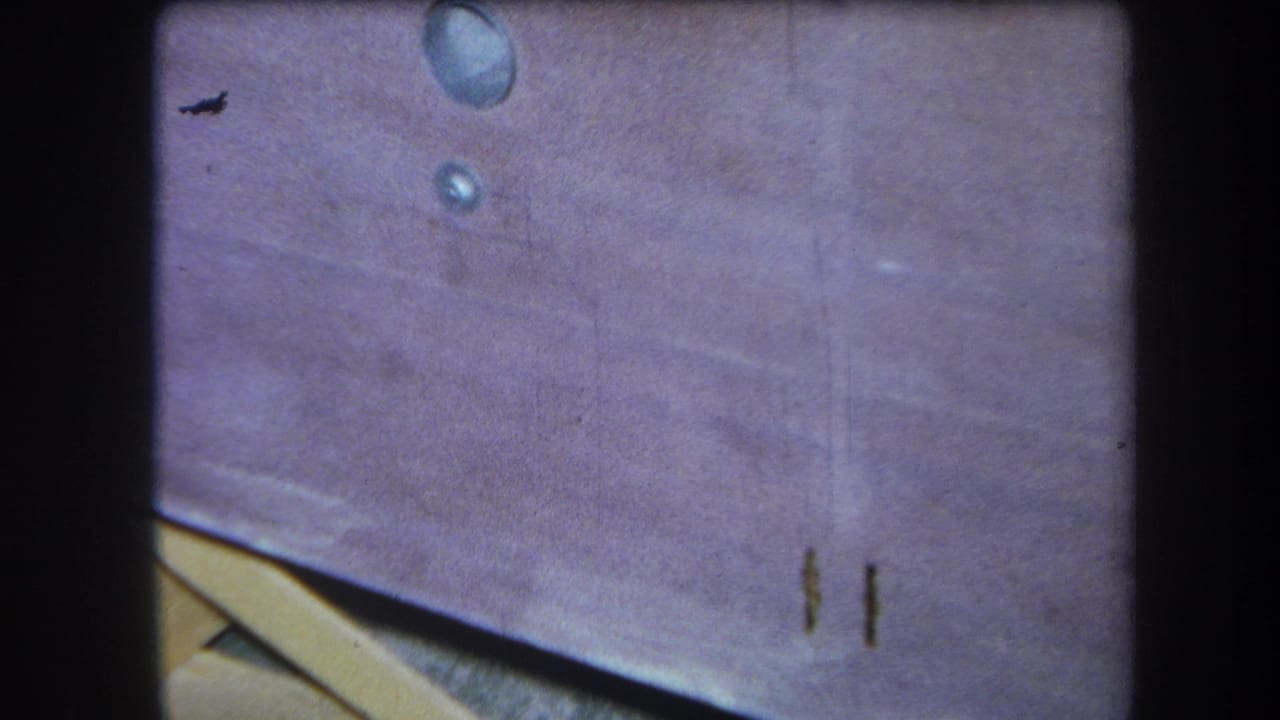 1964 8mm home-movie frame from Yucaipa showing a stained wooden picnic table surface with water spots, scratches, and soft focus.