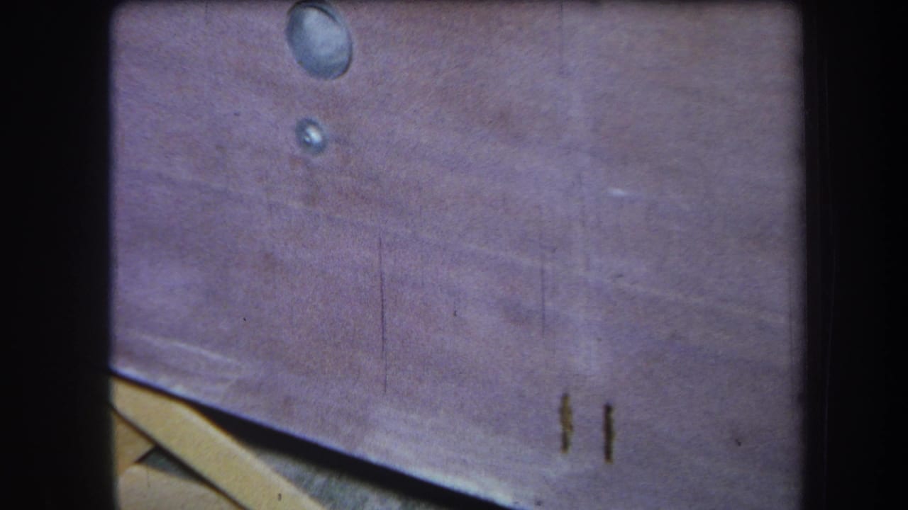 1964 Yucaipa home-movie close-up of a weathered picnic table surface with dark stains, soft grain, and visible gate edges.