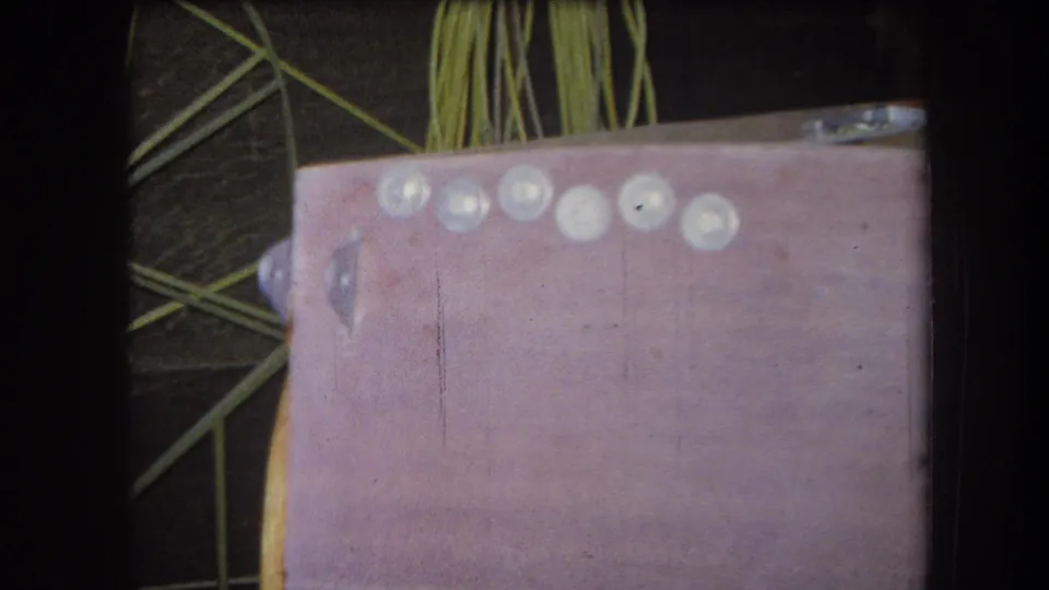 1964 Yucaipa-area 8mm frame showing a pink craft surface with pale round elements and green strands behind it.