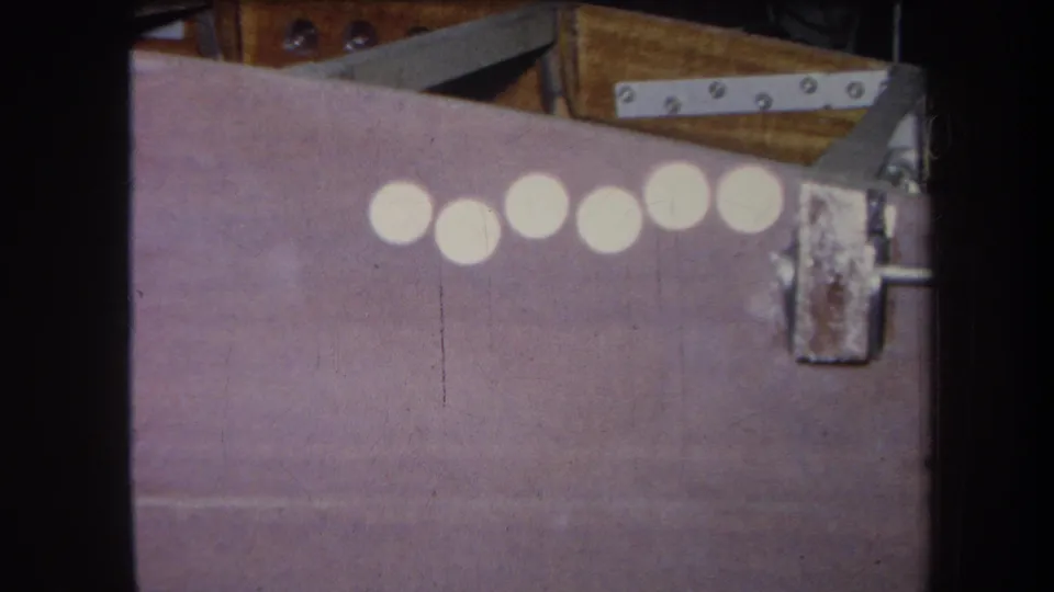 1964 8mm frame from Yucaipa showing six white circles across a purple-painted surface with rusty metal hardware and wood backing.