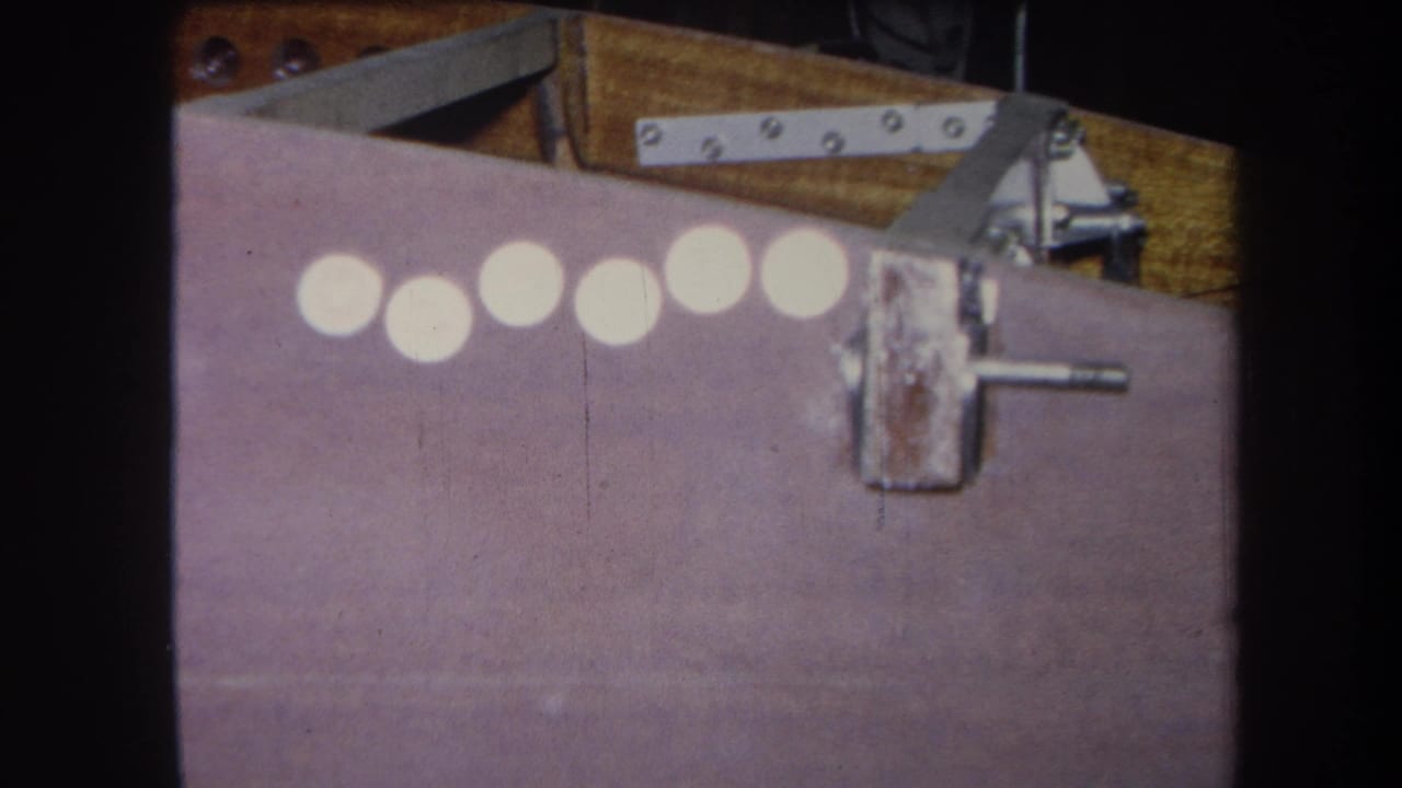 The frame holds on the same purple surface, with six pale circles, a worn latch, screws, and wood visible near the top edge.