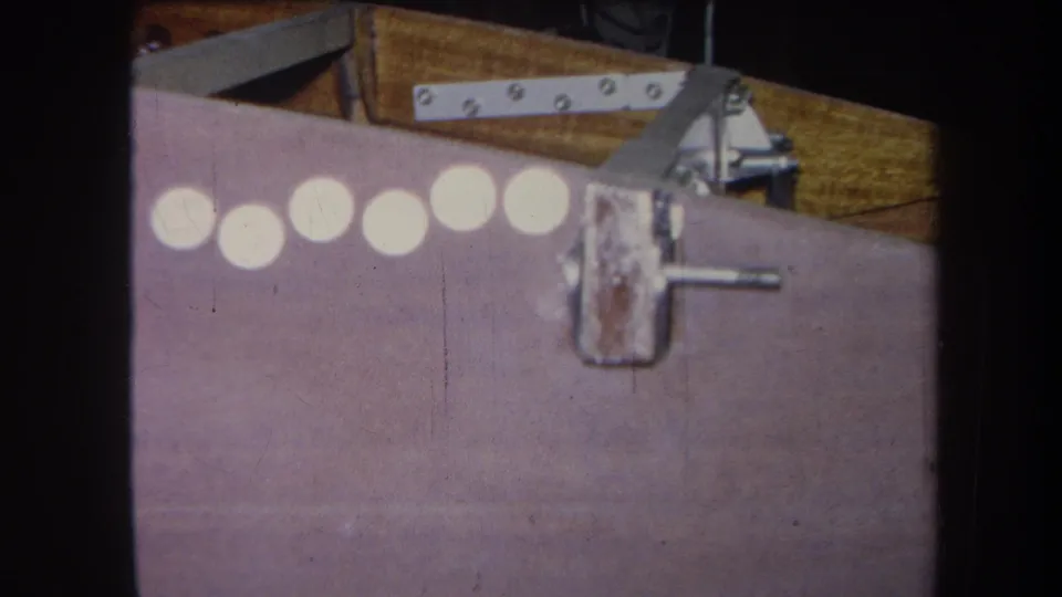 The 1964 home-movie frame shows the purple panel closer, with the row of circles partly cropped and a protruding metal rod near the latch.