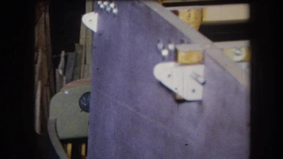 1964 8mm frame from Volmer Yucaipa showing a purple-painted wood structure with white brackets and stacked materials in back.