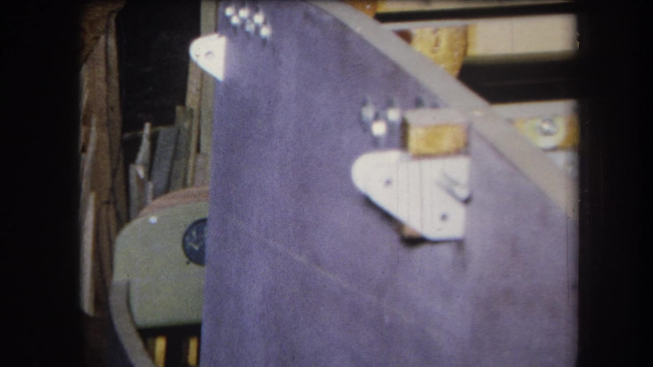 1964 Volmer Yucaipa home-movie frame with a purple wooden structure, white bracket hardware, and lumber visible behind it.