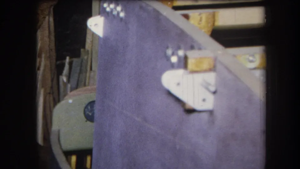 1964 Volmer Yucaipa home-movie frame with a purple wooden structure, white bracket hardware, and lumber visible behind it.