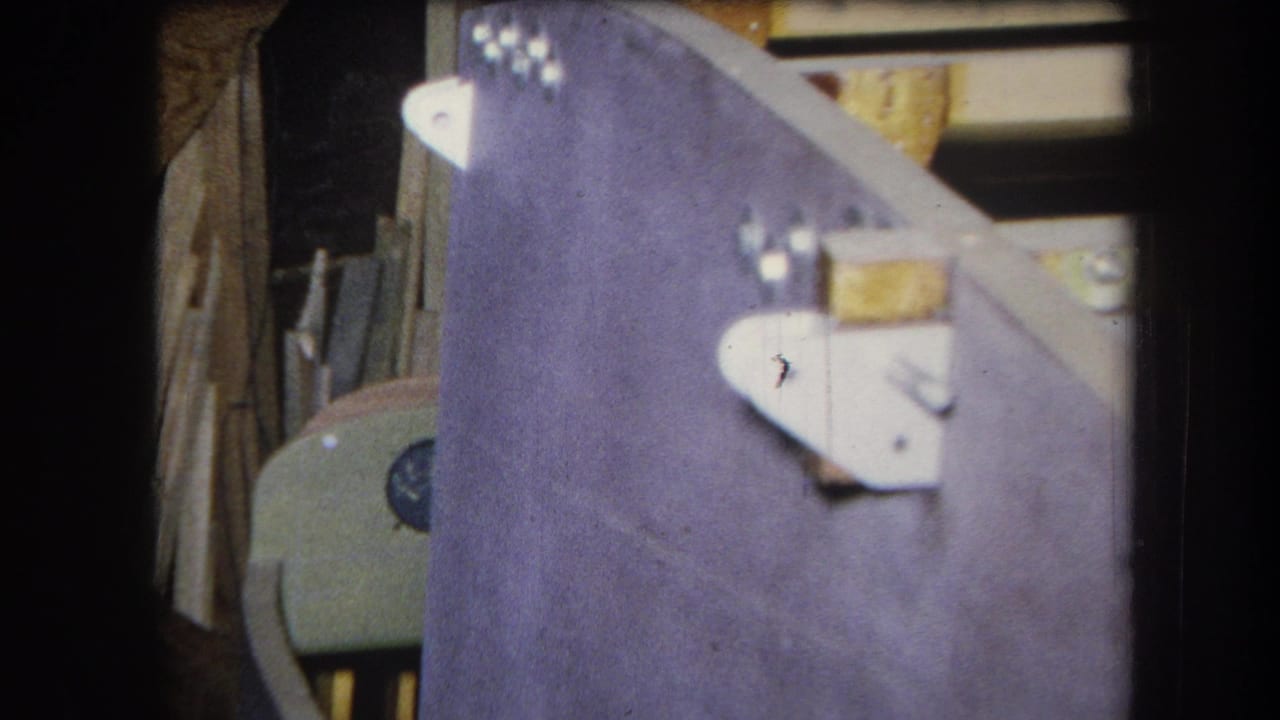 1964 8mm frame from Yucaipa showing a purple-painted wood panel with silver brackets, bolts, and surrounding workshop materials.