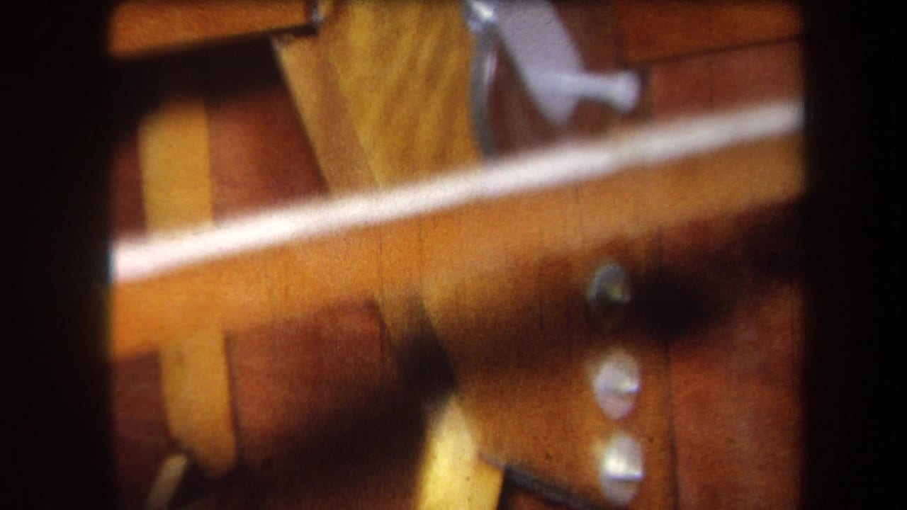 Close-up of varnished wooden parts with metal fittings and bolts, partly soft and cropped by film borders.