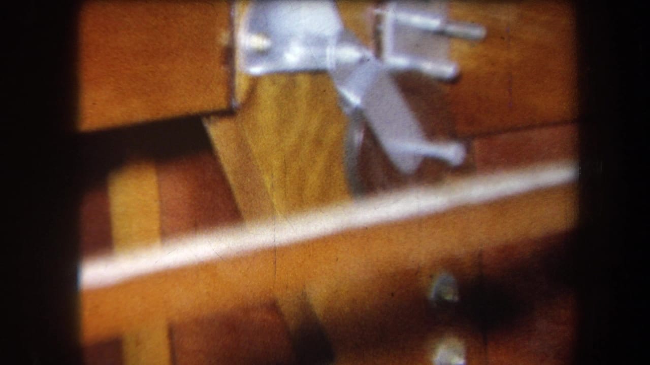 1964 8mm home-movie frame from Yucaipa showing wood panels, bolts, and metal fittings inside a small mechanical structure.