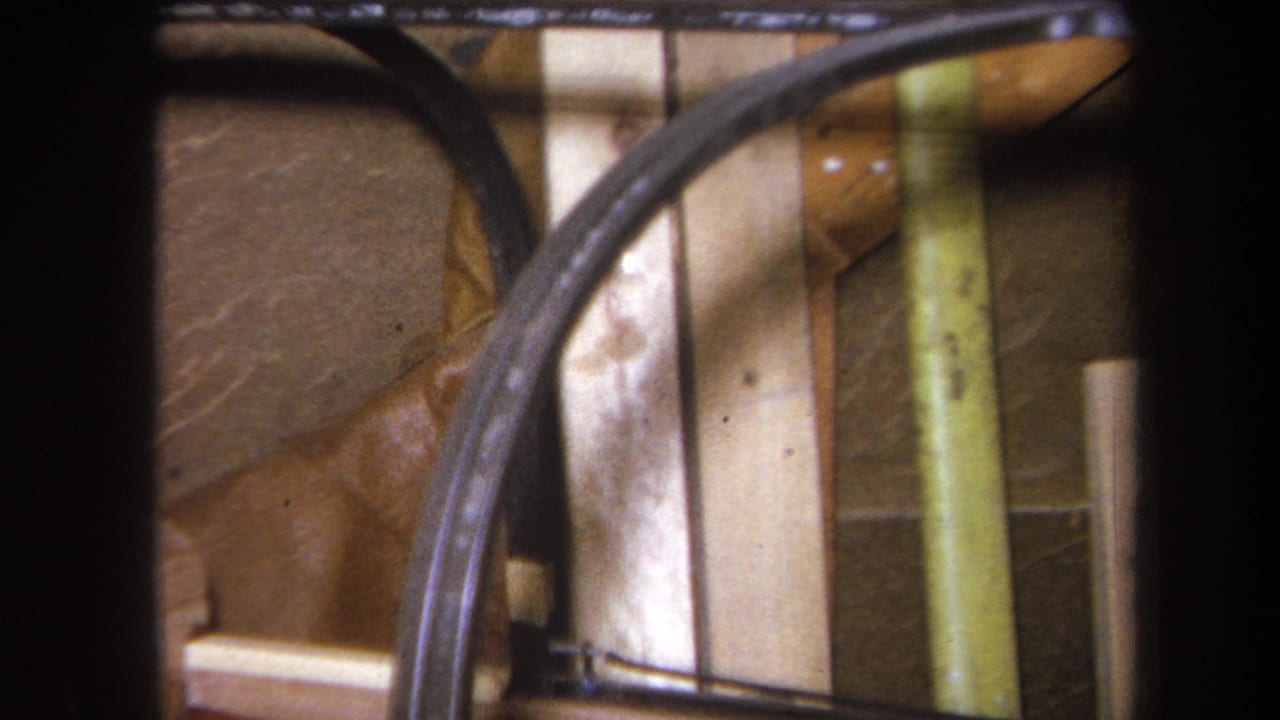 Close-up of curved tubing, wooden boards, and a vertical support inside a structure.