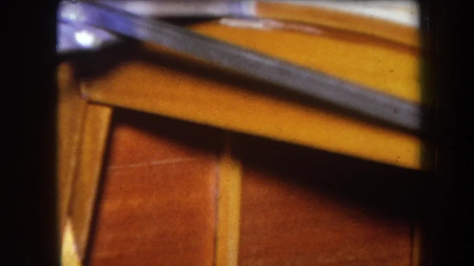 Close 1964 8mm view of an angled metal strip across warm wooden panels, with frame edges and shallow focus.