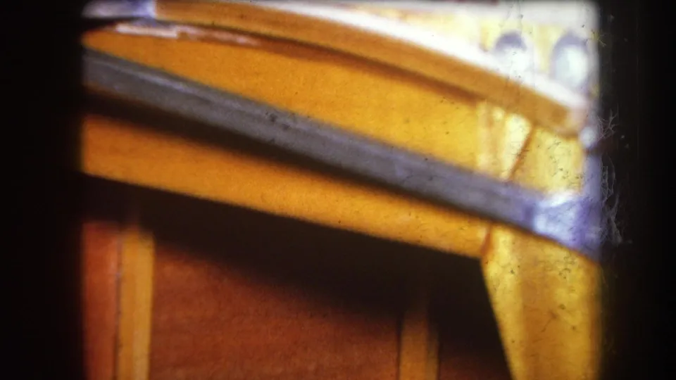 1964 8mm frame of a varnished wood corner and dark metal strip, with pale hardware partly visible near the upper edge.